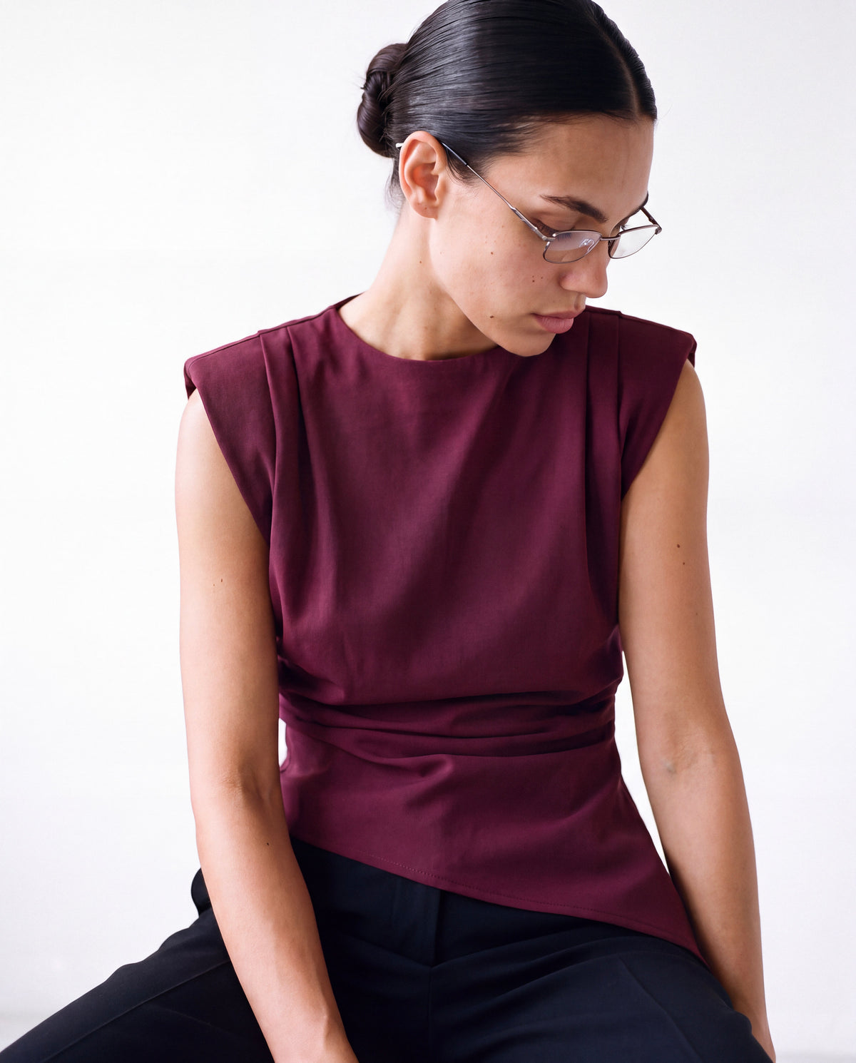 Padded-Shoulder Pleated Top in burgundy worn by model, seated