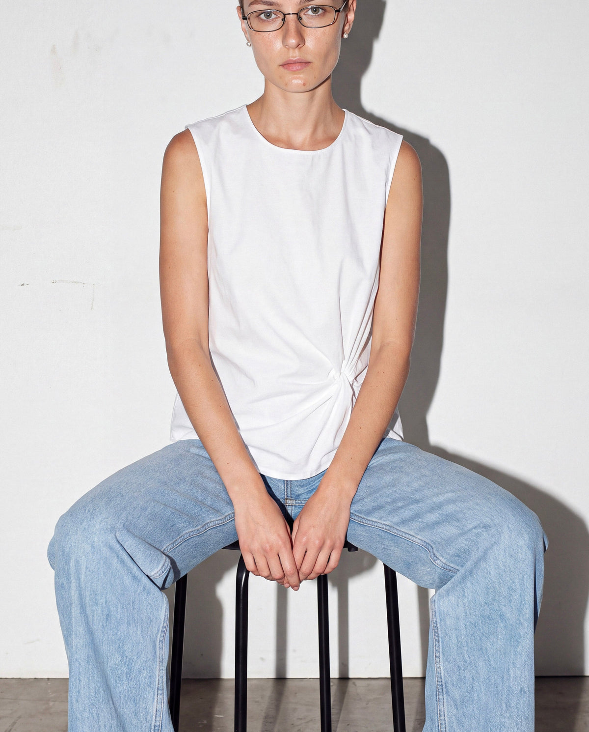 Pleated Sleeveless Top in white worn by model, seated