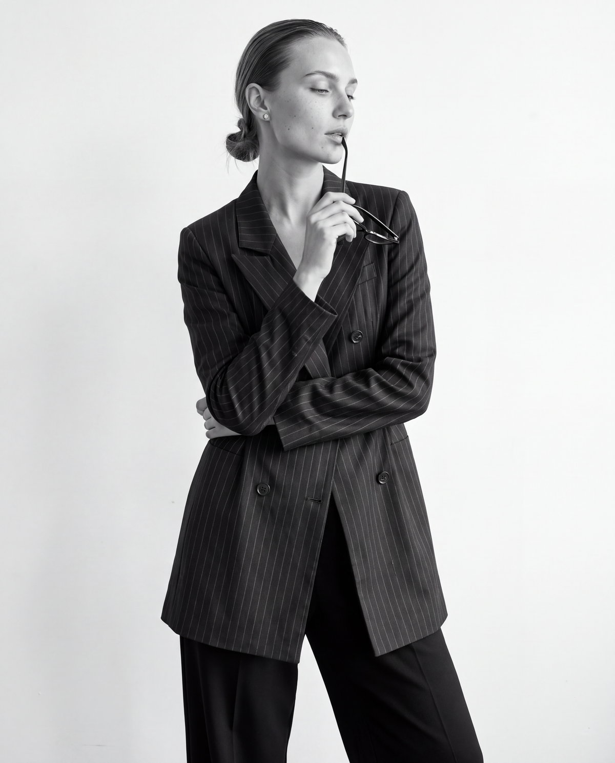 Model in a pinstripe blazer and black trousers, holding her glasses
